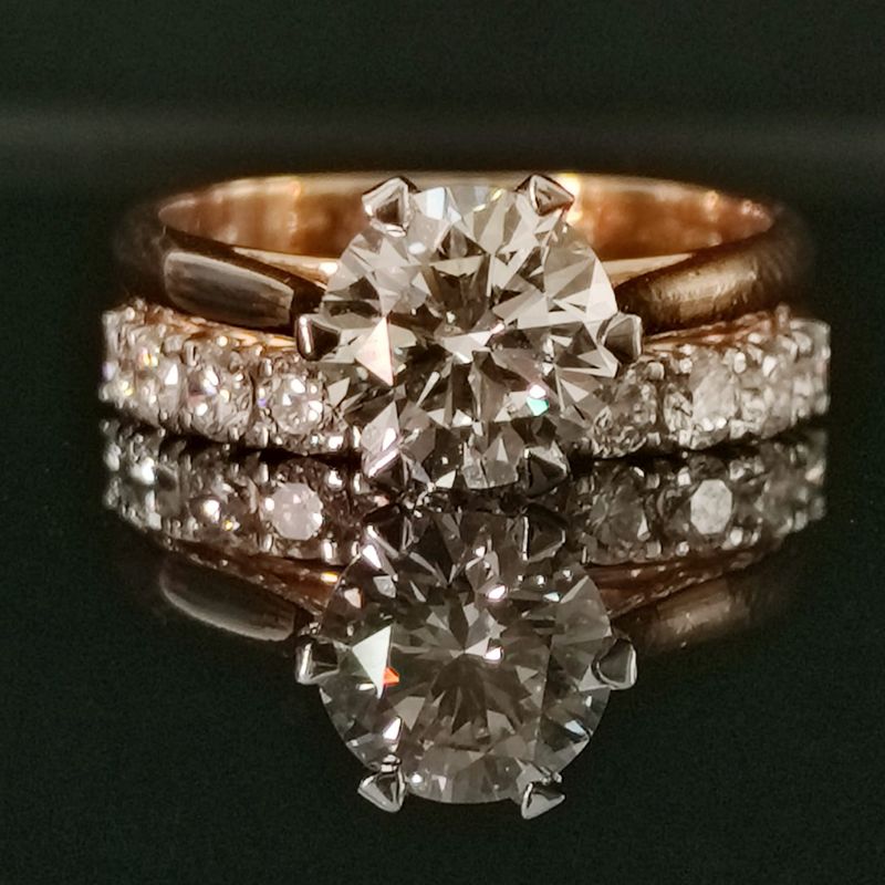 Rose gold ring with a large diamond and smaller diamonds on a reflective black surface